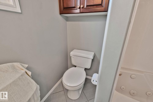 White toilet with tile flooring, wood-finish wall cabinetry, and a built-in tub with jets - 14724 73 Street Nw, Edmonton, AB 