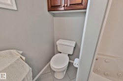 White toilet with tile flooring, wood-finish wall cabinetry, and a built-in tub with jets - 