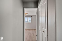 Neutral gray wall paint, doorway to a room with wood-finish flooring, white trim, and a window - 