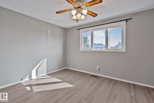 Light gray walls, wood-finish flooring, white trim, ceiling fan with integrated lighting, and a multi-pane window - 14724 73 Street Nw, Edmonton, AB 