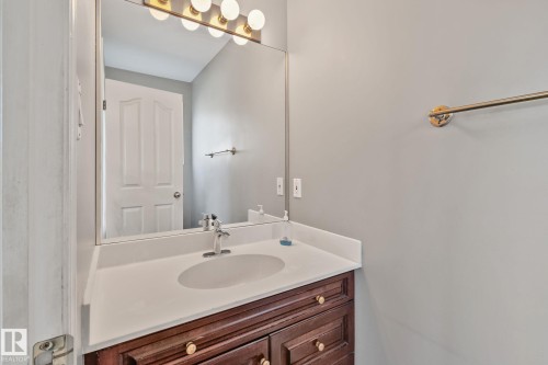 Vanity with a white countertop and integrated sink, chrome faucet, and a wood-finish cabinet with gold-tone hardware - 14724 73 Street Nw, Edmonton, AB 