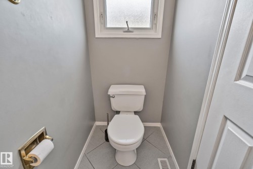 White paneled interior door, light grey wall paint, white toilet, frosted window, and grey tile flooring - 14724 73 Street Nw, Edmonton, AB 