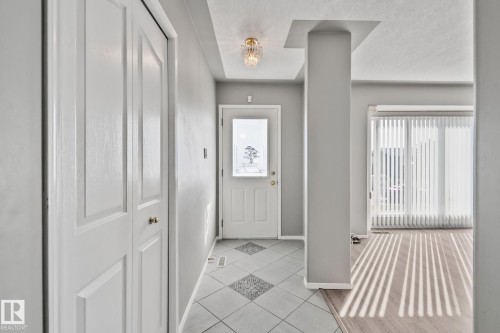 Entryway featuring tile flooring, white bi-fold doors, a translucent paneled door, a decorative ceiling fixture, and a structural column - 14724 73 Street Nw, Edmonton, AB 