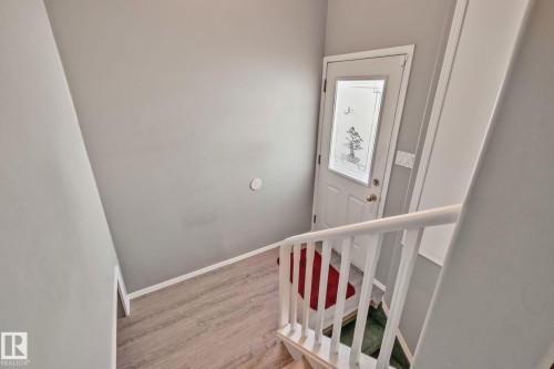 Entry door with decorative glass inlay, wood-finish flooring, and a white painted handrail - 14724 73 Street Nw, Edmonton, AB 