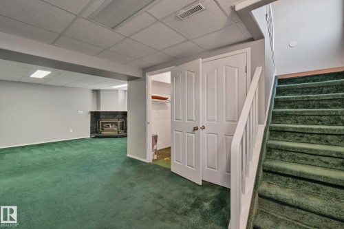 Finished lower level with a fireplace featuring a dark stone surround and mantel, green carpeting, white double doors, and a staircase with a white railing - 14724 73 Street Nw, Edmonton, AB 