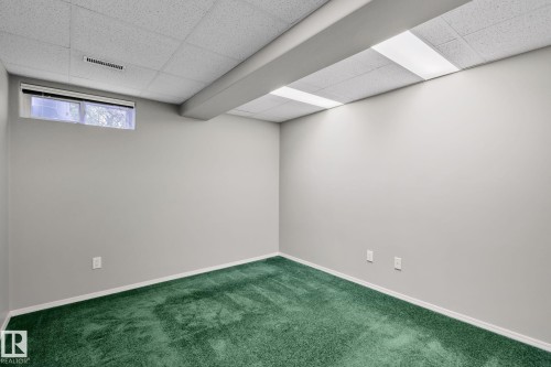 Room featuring green carpeting, light gray walls, a drop ceiling with integrated lighting, and a horizontal window - 14724 73 Street Nw, Edmonton, AB 