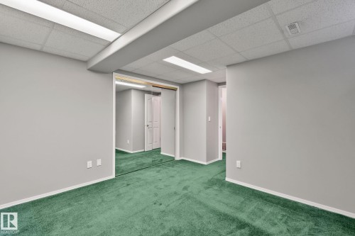 Wall-to-wall green carpeting with light gray walls, suspended ceiling panels, and built-in mirrored closet doors - 14724 73 Street Nw, Edmonton, AB 