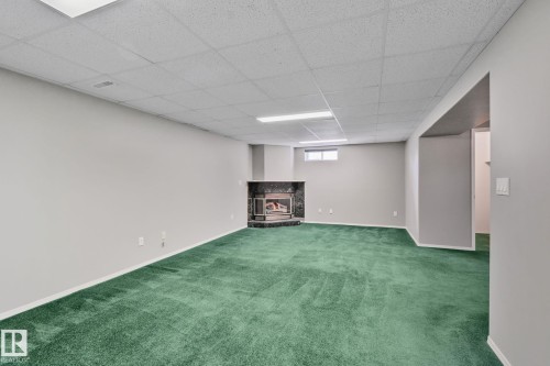 Recessed corner fireplace with a dark stone surround, light gray painted walls, a dropped ceiling, and a single window - 14724 73 Street Nw, Edmonton, AB 