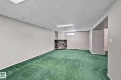 Recessed corner fireplace with a dark stone surround, light gray painted walls, a dropped ceiling, and a single window - 