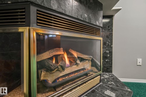Fireplace featuring black stone surround, brass-finish trim, and protective glass - 14724 73 Street Nw, Edmonton, AB 