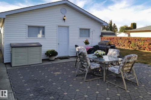 Paved patio with decorative paver pattern, white vinyl siding exterior, and a mature hedge - 14724 73 Street Nw, Edmonton, AB 