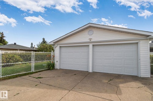 Detached two-car garage with panel-style doors and white vinyl siding, featuring a gabled roofline and an exterior light fixture - 14724 73 Street Nw, Edmonton, AB 