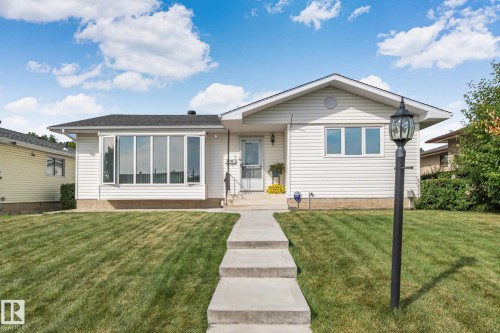 White siding exterior with a dark shingle roof, featuring a bay window, a concrete walkway, and a decorative lamppost - 14724 73 Street Nw, Edmonton, AB 
