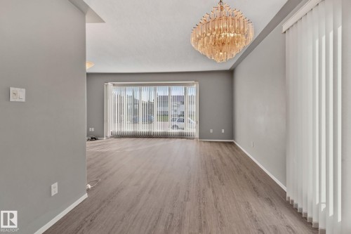 Spacious room featuring wood-finish flooring, a large window with vertical blinds, and a decorative ceiling fixture - 14724 73 Street Nw, Edmonton, AB 