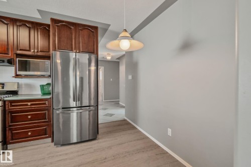 Kitchen featuring rich wood cabinetry, stainless steel refrigerator, built-in microwave, a gas range, and wood-finish flooring - 14724 73 Street Nw, Edmonton, AB 
