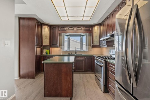 Kitchen featuring wood-finish cabinetry, stainless steel appliances, a center island with a countertop, and a bay window - 14724 73 Street Nw, Edmonton, AB 