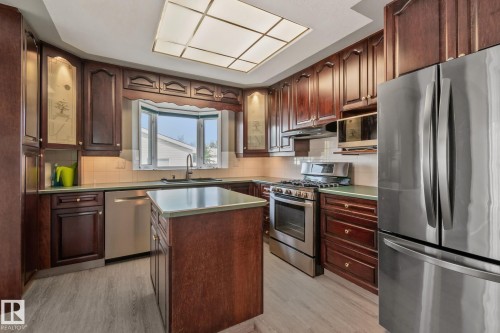 Kitchen featuring wood-finish cabinetry, stainless steel appliances, a center island with a countertop, a bay window, and a grid ceiling light fixture - 14724 73 Street Nw, Edmonton, AB 