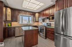Kitchen featuring wood-finish cabinetry, stainless steel appliances, a center island with a countertop, a bay window, and a grid ceiling light fixture - 