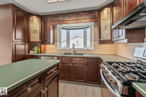 Dark wood-finish cabinetry, bay window, stainless steel appliances, solid surface countertops, and light wood-finish flooring - 14724 73 Street Nw, Edmonton, AB 