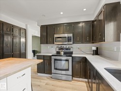 Modern kitchen featuring dark cabinetry, stainless steel appliances, light countertops, and a subway tile backsplash - 