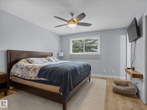 Spacious room featuring light blue walls, wood-finish flooring, a ceiling fan with integrated lighting, and a horizontal window with blinds - 4 Lovatt Place, St. Albert, AB - Indoor Photo Showing Bedroom