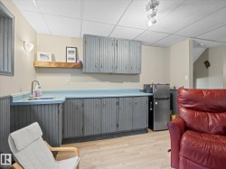 Lower-level space featuring a built-in wet bar with a stainless steel sink, light blue countertop, and gray paneled cabinetry - 