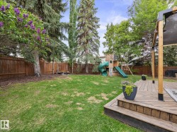Spacious backyard featuring a wooden deck with a pergola, a large lawn, a privacy fence, mature trees, and an outdoor play structure - 