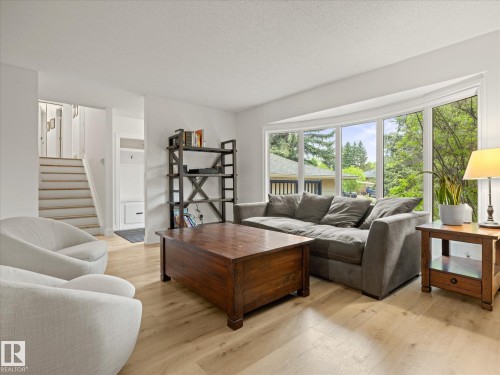 Living area featuring light wood-finish flooring, a large bay window, white painted walls, and a visible staircase with white risers and light wood treads - 4 Lovatt Place, St. Albert, AB - Indoor Photo Showing Living Room