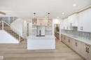 Gourmet kitchen featuring a central island, wood-finish flooring, full-height cabinetry, geometric tile backsplash, and a staircase with wood railing and black spindles - 13144 187 Avenue Nw, Edmonton, AB 