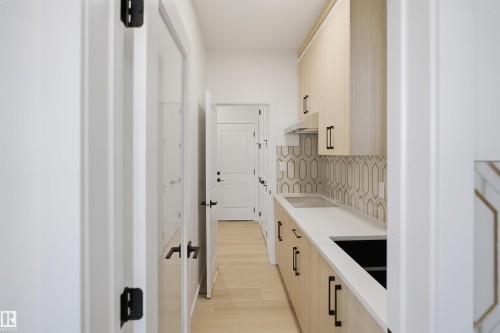 Light wood-finish cabinetry with black hardware, white countertops, integrated sink, patterned backsplash, and wood-finish flooring - 13144 187 Avenue Nw, Edmonton, AB 
