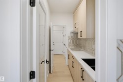 Light wood-finish cabinetry with black hardware, white countertops, integrated sink, patterned backsplash, and wood-finish flooring - 