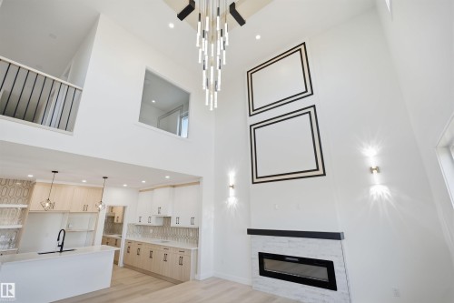 Two-story living area with high ceilings, linear electric fireplace with stone surround, a contemporary chandelier, and a black metal railing - 13144 187 Avenue Nw, Edmonton, AB 