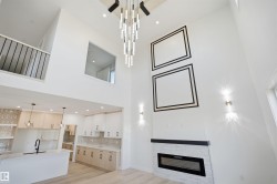 Two-story living area with high ceilings, linear electric fireplace with stone surround, a contemporary chandelier, and a black metal railing - 