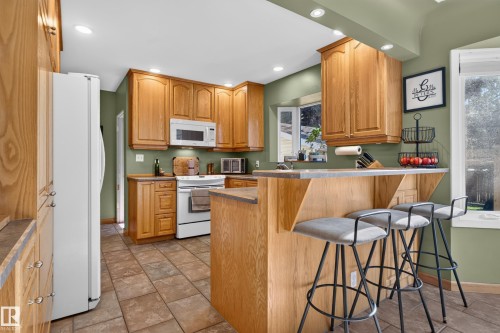 Wood cabinetry, built-in microwave, tile flooring, bay window, and a breakfast bar with counter seating - 14611 109 Avenue Nw, Edmonton, AB 