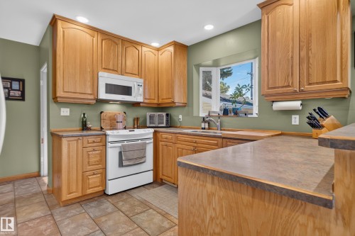 Kitchen featuring wood cabinetry, stone-look countertops, a built-in microwave, and a bay window - 14611 109 Avenue Nw, Edmonton, AB 