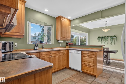 Kitchen featuring light wood cabinetry, countertop range, stainless steel sink, bay window, and tile flooring - 14611 109 Avenue Nw, Edmonton, AB 