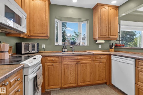 Kitchen featuring wood cabinetry, a bay window, a stainless steel microwave, a built-in dishwasher, and a black cooktop - 14611 109 Avenue Nw, Edmonton, AB 