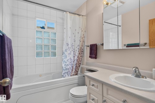 Built-in bathtub with tiled surround, glass block window, chrome faucet, vanity with integrated sink, and mirror with overhead lighting - 14611 109 Avenue Nw, Edmonton, AB 