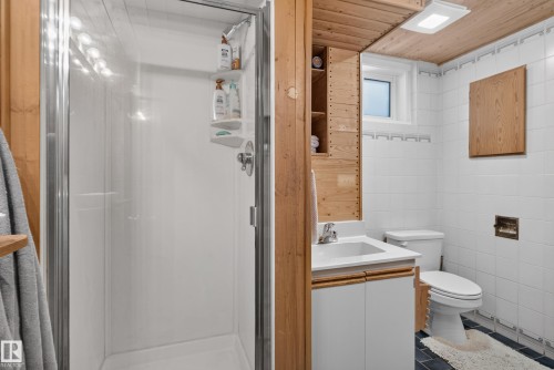 Enclosed shower with clear glass door, wood-paneled ceiling, white tiled walls, vanity with built-in storage, and a single window - 14611 109 Avenue Nw, Edmonton, AB 