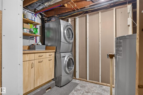 Stackable laundry appliances, wood-finish cabinetry, built-in shelving, laminate countertop, and water heater - 14611 109 Avenue Nw, Edmonton, AB 