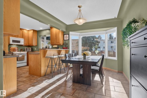 Kitchen and dining area featuring wood cabinetry, a breakfast bar, a bay window, and tile flooring - 14611 109 Avenue Nw, Edmonton, AB 