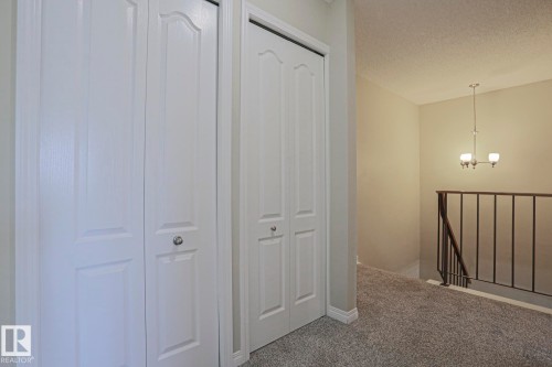 White bi-fold closet doors, textured carpet flooring, and a wrought iron stair railing - 319 Telford Court, Leduc, AB 
