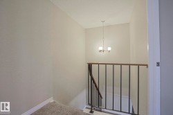 Staircase featuring carpeted steps, wrought iron railing with wood-finish top, and a ceiling-mounted chandelier - 