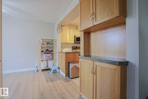 Wood-finish flooring throughout, light neutral wall paint, built-in cabinetry with a dark countertop, white tiled kitchen backsplash, and stainless steel appliances - 319 Telford Court, Leduc, AB 