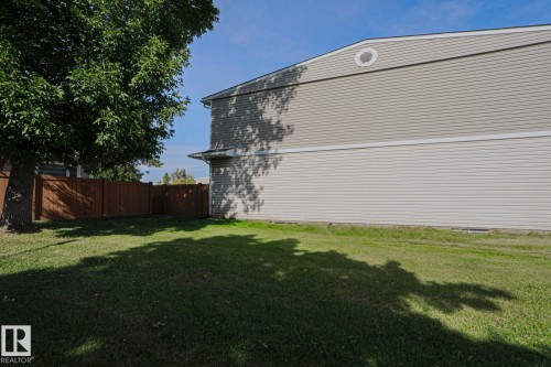Manicured lawn with mature tree, brown privacy fencing, and grey horizontal siding - 319 Telford Court, Leduc, AB 