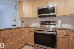 Wood-finish cabinetry, stainless steel oven, stainless steel microwave, stone-look countertops, and white tile backsplash - 