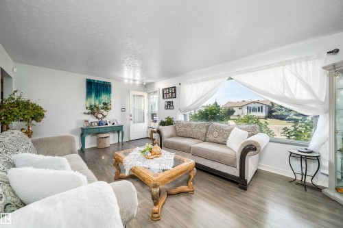Spacious living area featuring wood-finish flooring, a large picture window, and a front entry door with decorative glass - 10245 160 Street Nw, Edmonton, AB 