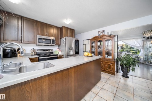 Kitchen featuring wood cabinetry, stainless steel appliances, light-toned countertops, and tile flooring - 10245 160 Street Nw, Edmonton, AB 
