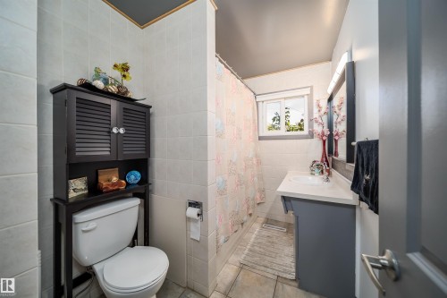 White tiled walls and flooring, complemented by a vanity with an integrated sink and a window providing natural light - 10245 160 Street Nw, Edmonton, AB 