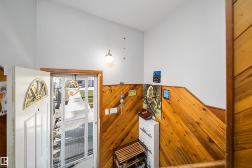 Angled wood-paneled wall, white entry door with an arched window, white walls, and a wall-mounted light fixture - 10245 160 Street Nw, Edmonton, AB 